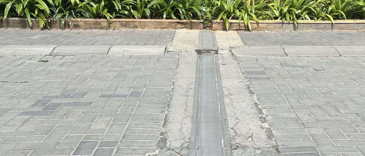 A floor expansion joint crossing a paved podium, with planting and towers beyond, Bengaluru